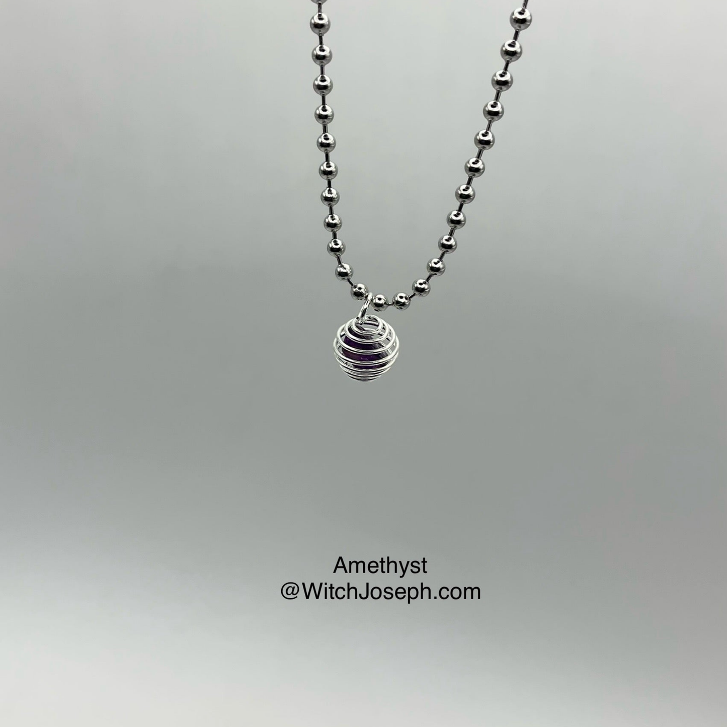 Silver tone necklace with a small cage pendant with amethyst chip inside on a gray background