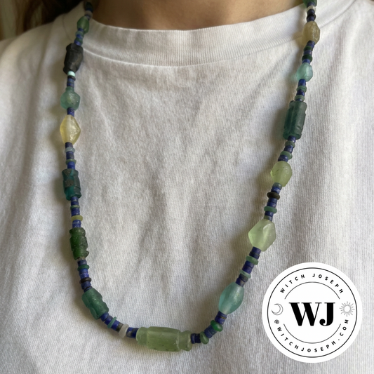 Necklace with ancient Roman glass green and blue beads with lapis beads displayed on a model in a white shirt, featuring the Witch Joseph logo