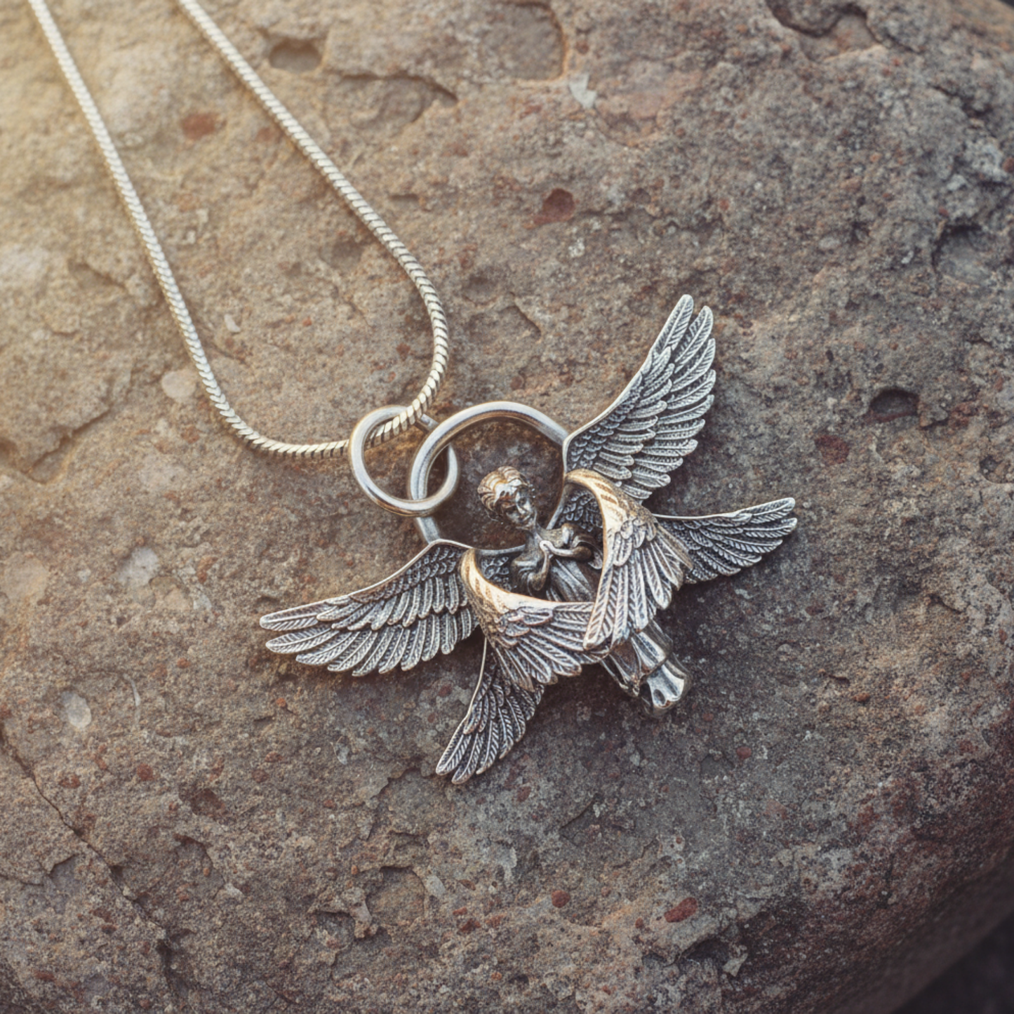 Silver tone angel pendant necklace displayed on a rustic stone surface