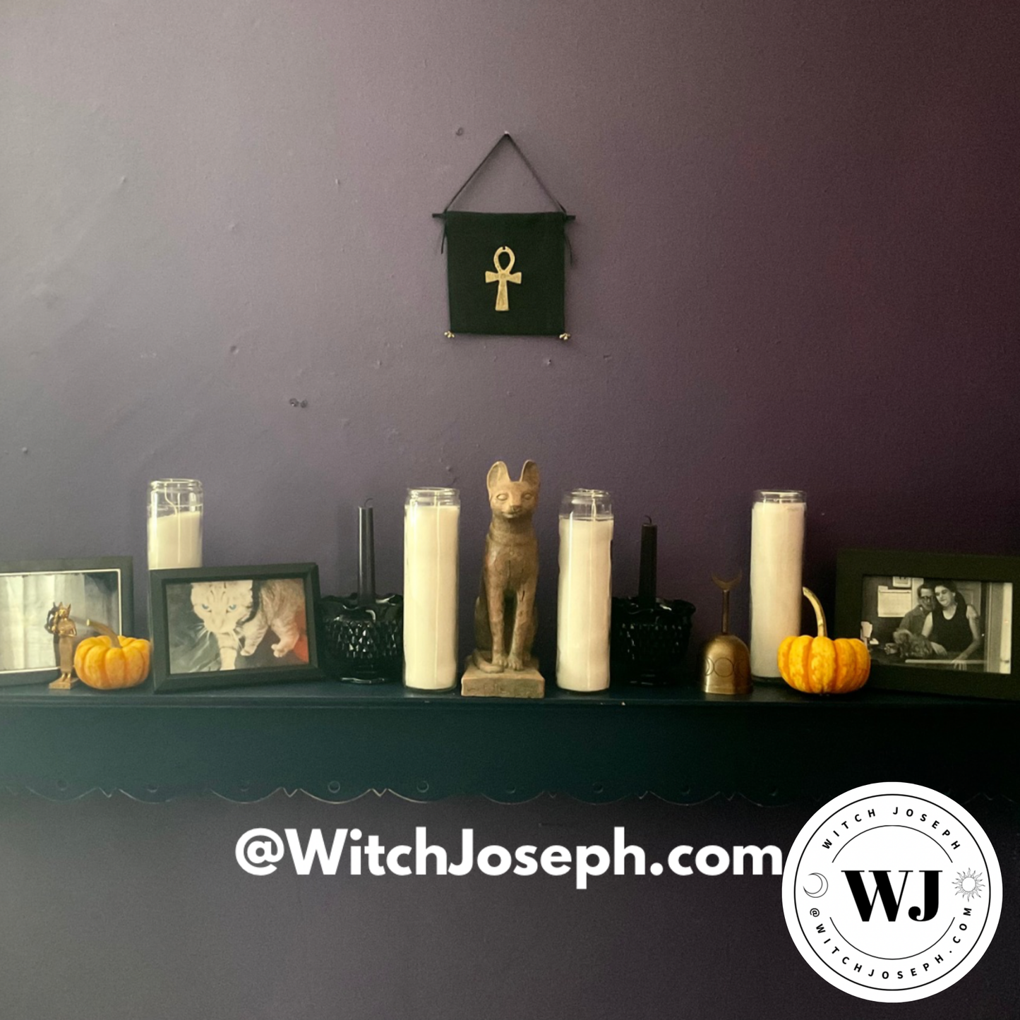 Ancestor shrine shelf decorated with candles, pumpkins, and a Bastet cat statue against a purple wall…hanging above is the Ankh Wall hanging