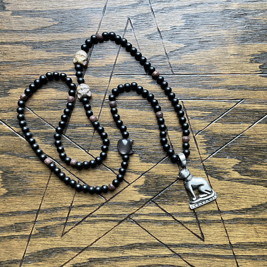Black beaded Bastet necklace with a silver tone Bastet pendant displayed on a wooden surface with a pentagram etched in to it