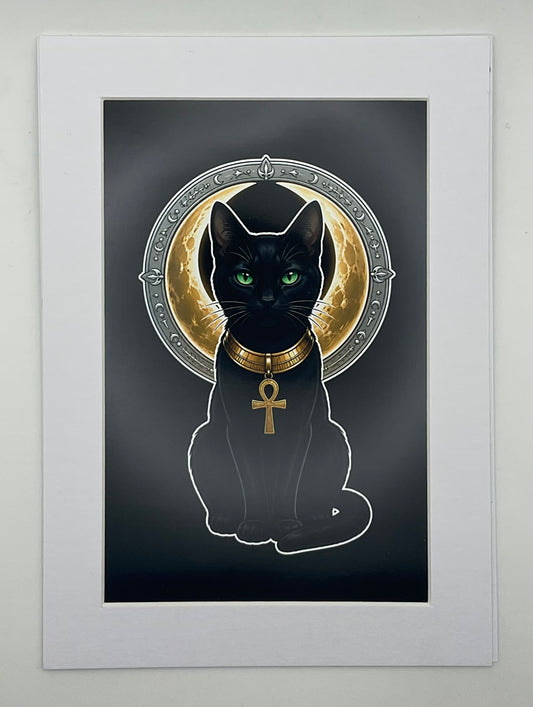 A matted art print featuring a black cat Bastet with glowing green eyes, wearing a gold collar with an ankh pendant, set against a dark background with a circular gold and silver halo motif. The print is mounted in a white Mat.