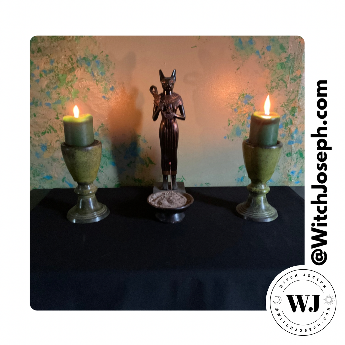 Statue of a deity between two lit candles on a black altar cloth with a textured wall background.