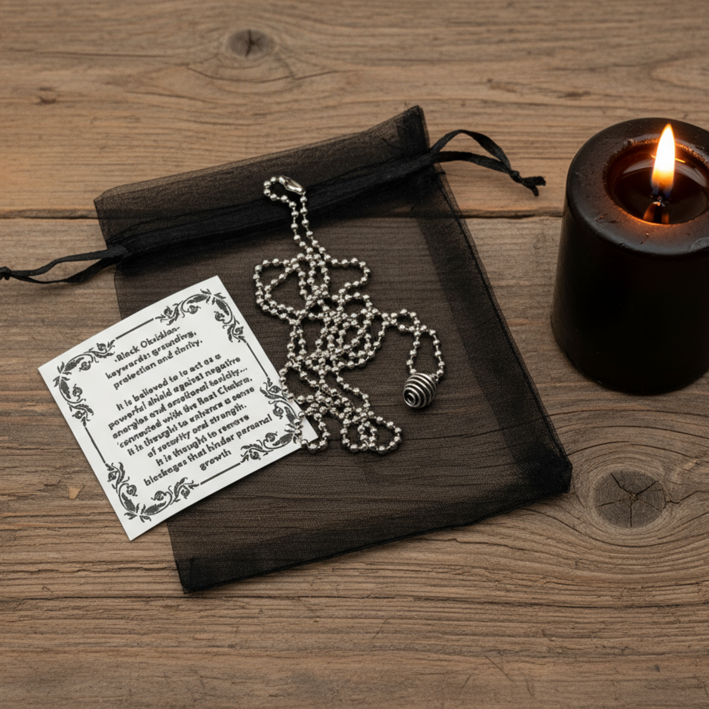 Necklace with black obsidian cage pendant next to a black candle on a wooden surface