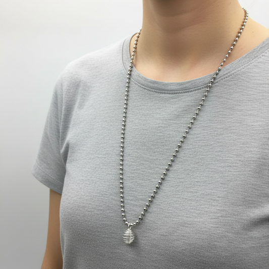 Person wearing a silver tone ball chain necklace with a clear quartz chip in cage pendant on a plain background