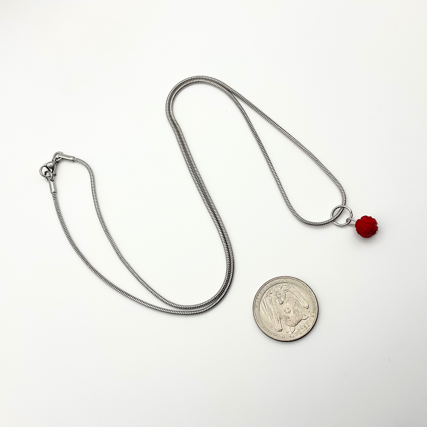 Silver tone necklace with a red coral pendant next to a coin on a white background