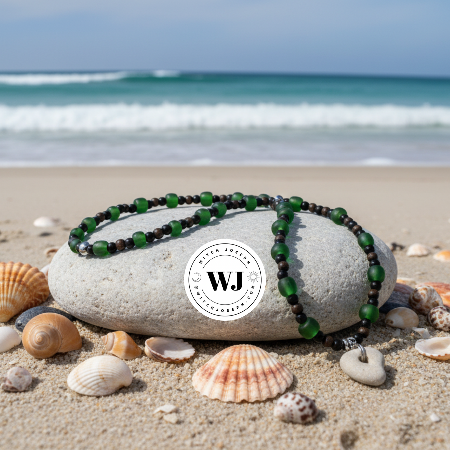 Green beaded necklace with Holey Stone…with green and black and copper accent beads displayed on a rock with seashells and ocean waves in the background, featuring the WJ brand logo.