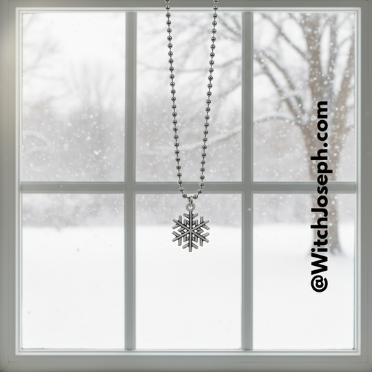 Snowflake charm necklace hanging in front of a window with a snowy scene