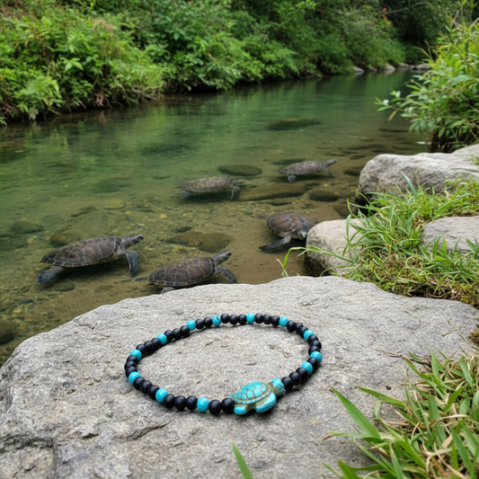 Black and turquoise tone stretch Bracelet with turtle bead laying on a rock by a stream with turtles in the background