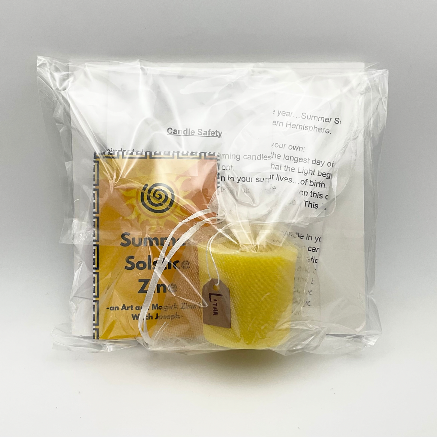 Packaged yellow Summer Solstice candle with Zine and other contents seen through the transparent back of the package.