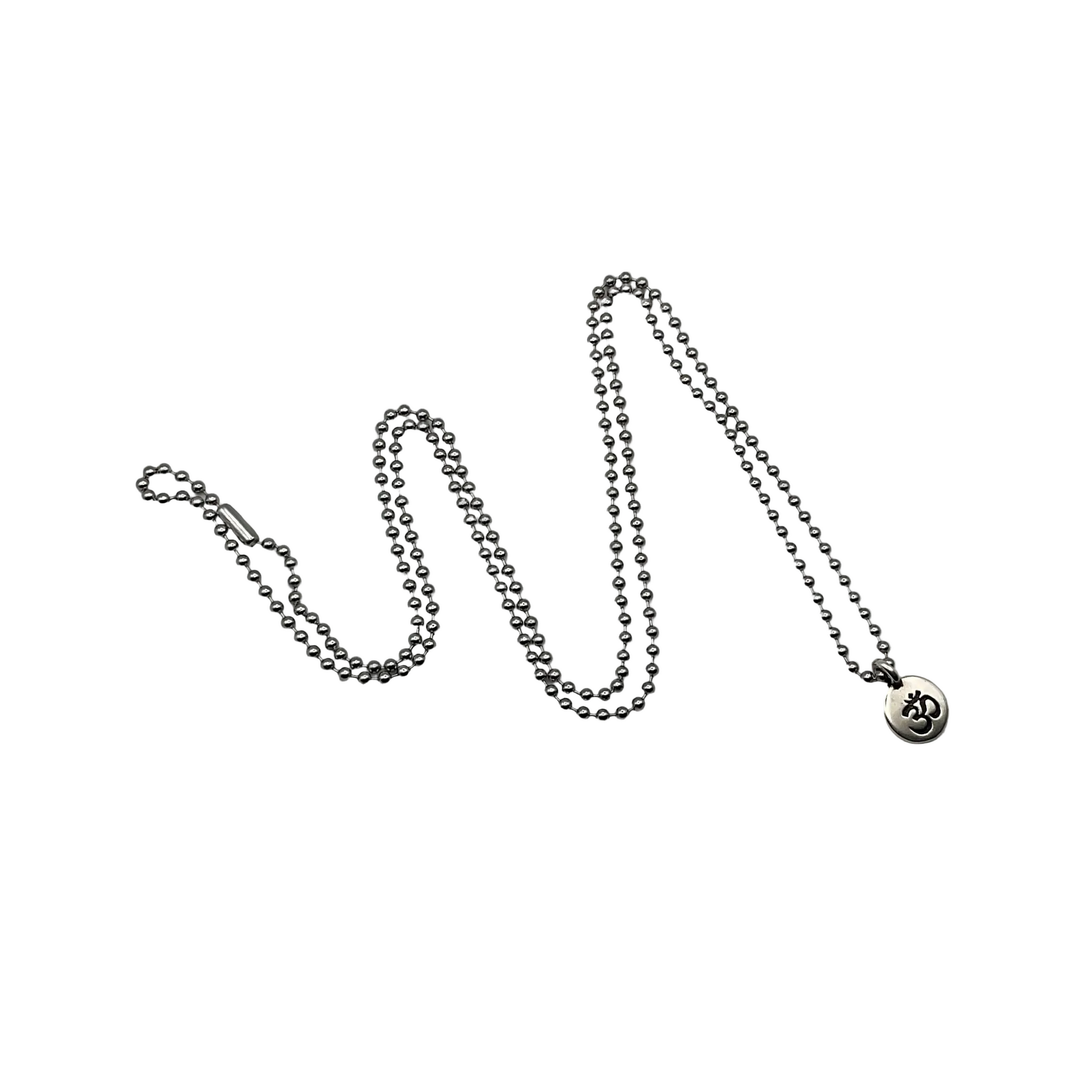 Silver necklace with a small round pendant with the Sanskrit OM or AUM on it on a silver tone ball chain on a white background