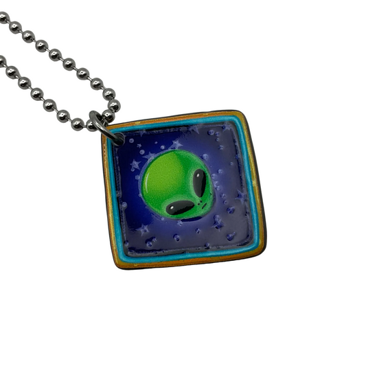 Square pendant with green alien design on a ball chain against a white background