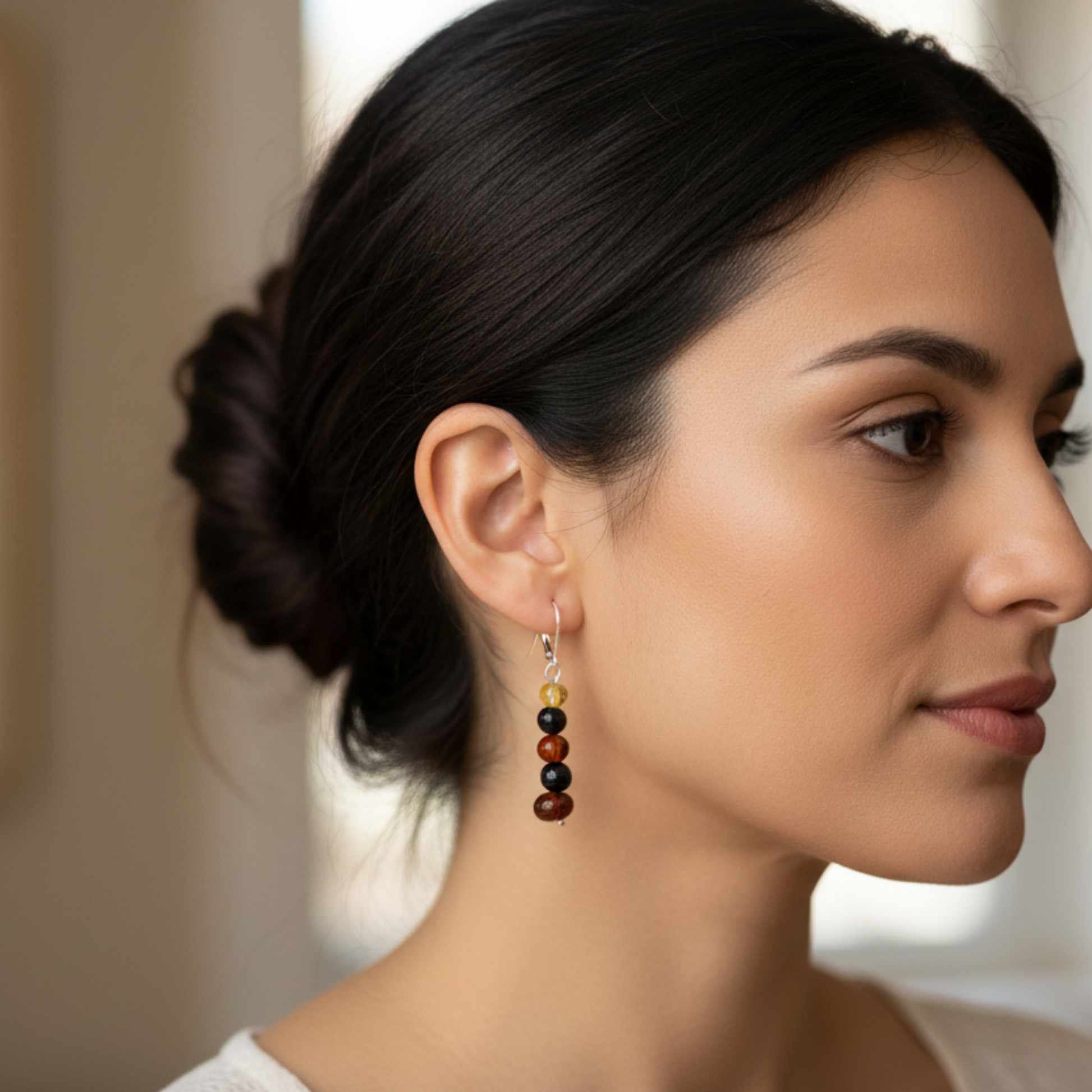 Woman wearing a set of dangling earrings with amber and jet beads on sterling silver attachment