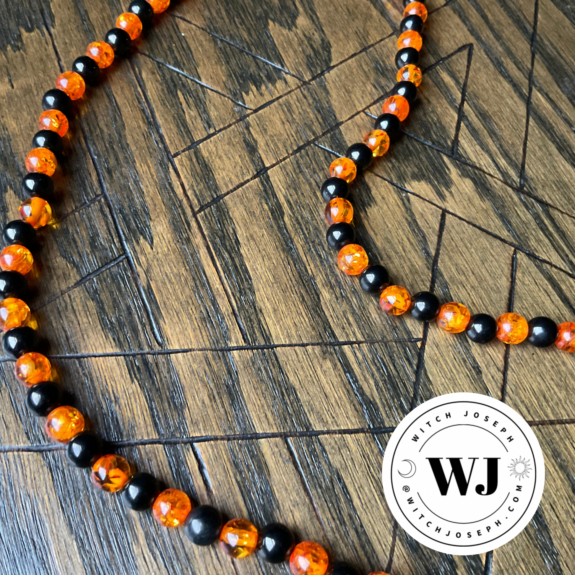A black and orange, jet and amber, necklace displayed on wood with an etched pentagram and the Witch Joseph logo