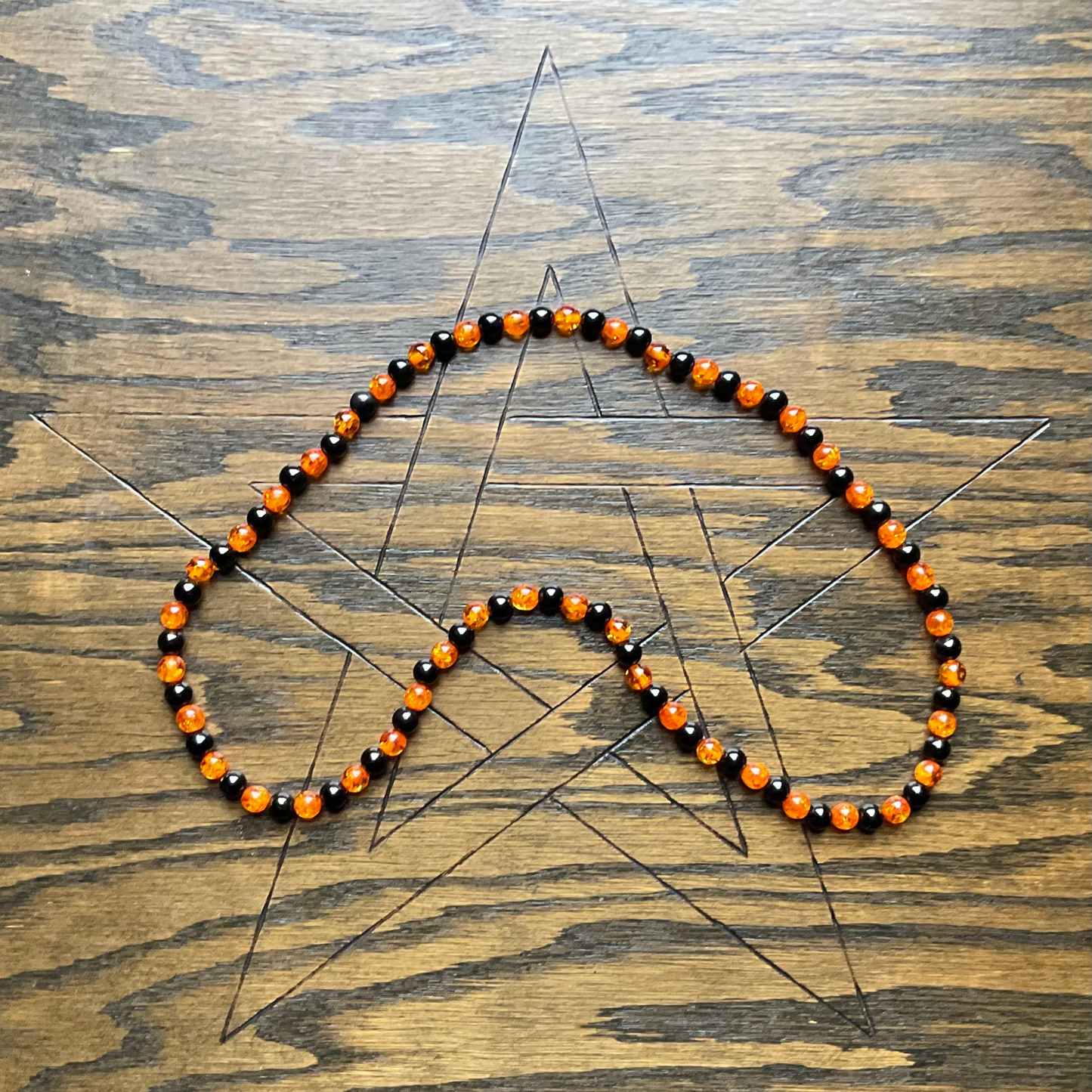 Necklace with large amber orange and jet black beads displayed on a wooden surface with an etched pentagram.