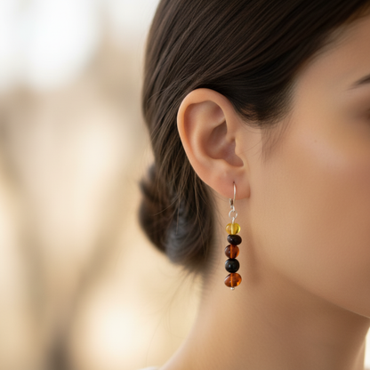 Close-up of an ear wearing a colorful Baltic Amber and Russian Jet beaded sterling silver earring with a blurred background