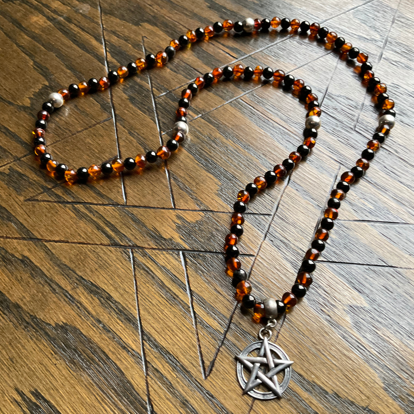 Amber and Jet Necklace with beaded chain and sterling pentagram pendant with sterling bead accents shown on a wooden surface.