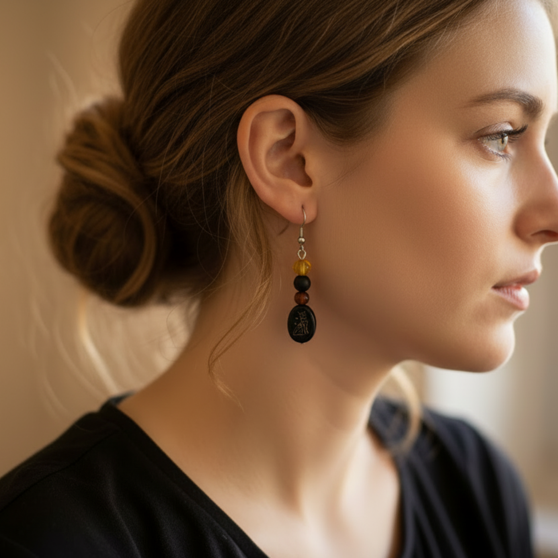 the Bastet Baltic amber and Russian jet earrings with glass cat glyph bead, shown being worn here from the side on a woman’s ear