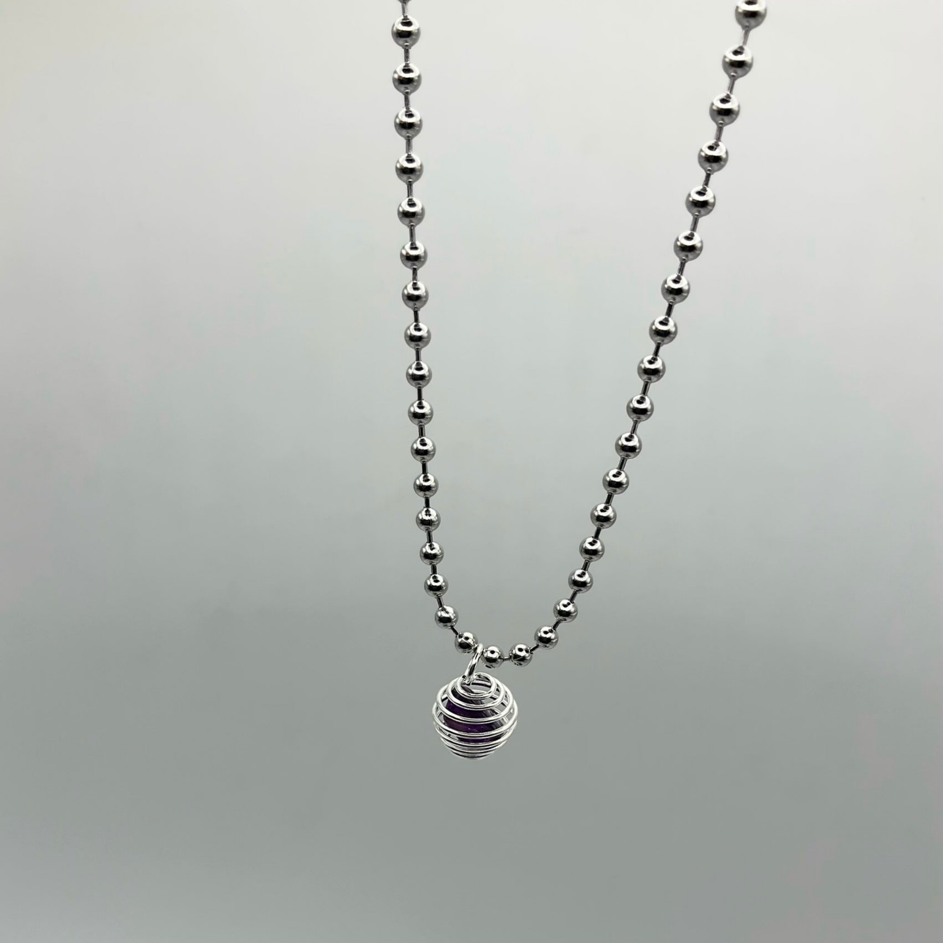 Silver ball chain necklace with an amethyst chip cage pendant on a light gray background
