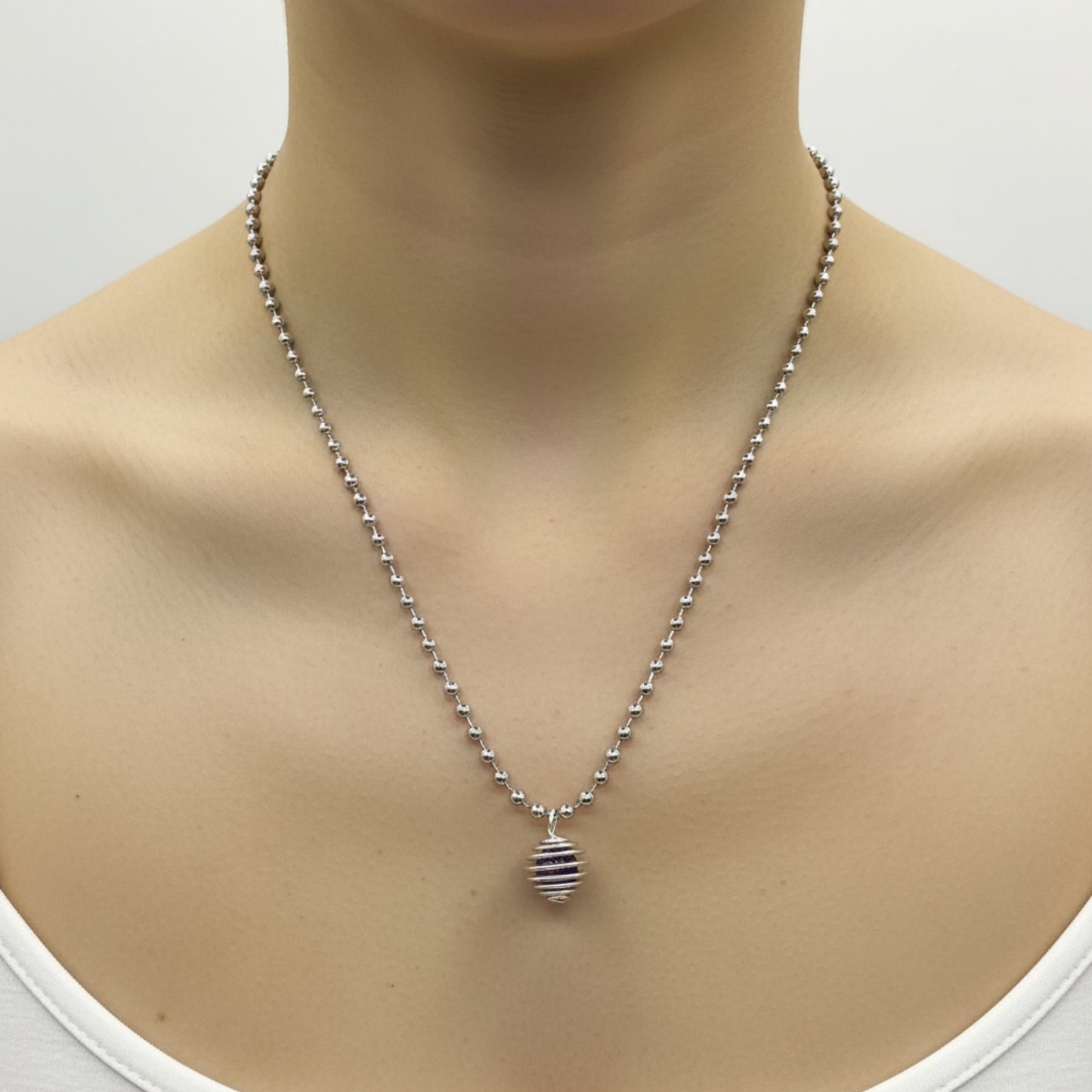 Silver tone necklace with an amethyst chip cage pendant being worn by a person