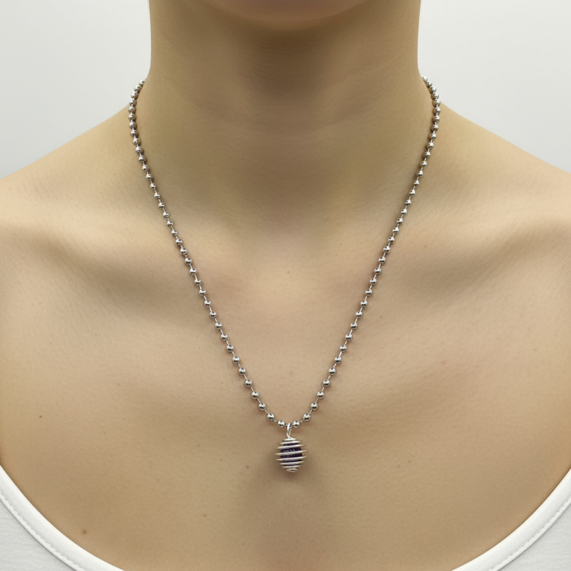 Silver tone necklace with an amethyst chip cage pendant being worn by a person