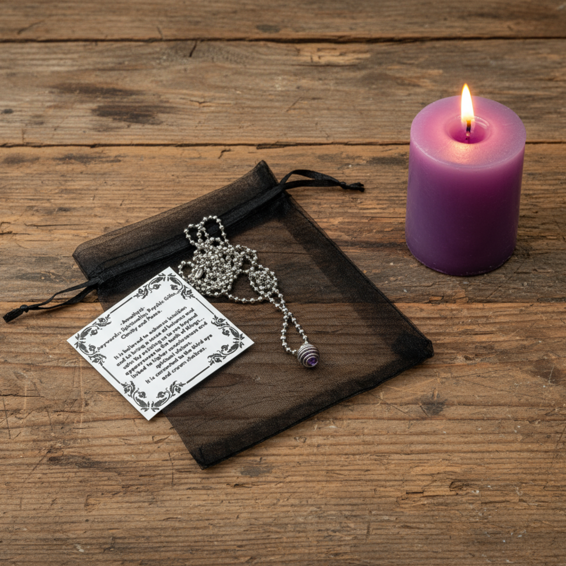 Necklace with amethyst chip in cage pendant and purple candle on wooden surface