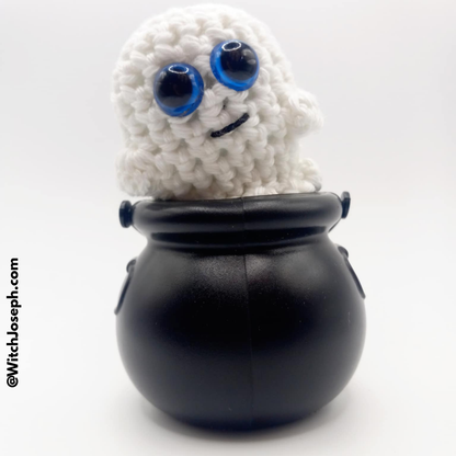 White Amigurumi Ghost glows in dark with blue eyes inside a black cauldron on a white background with the Witch Joseph URL