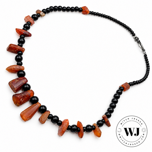 A display against a white background of an antique carnelian bead necklace with contemporary black beads…shown with the Witch Joseph logo in the lower right hand corner.