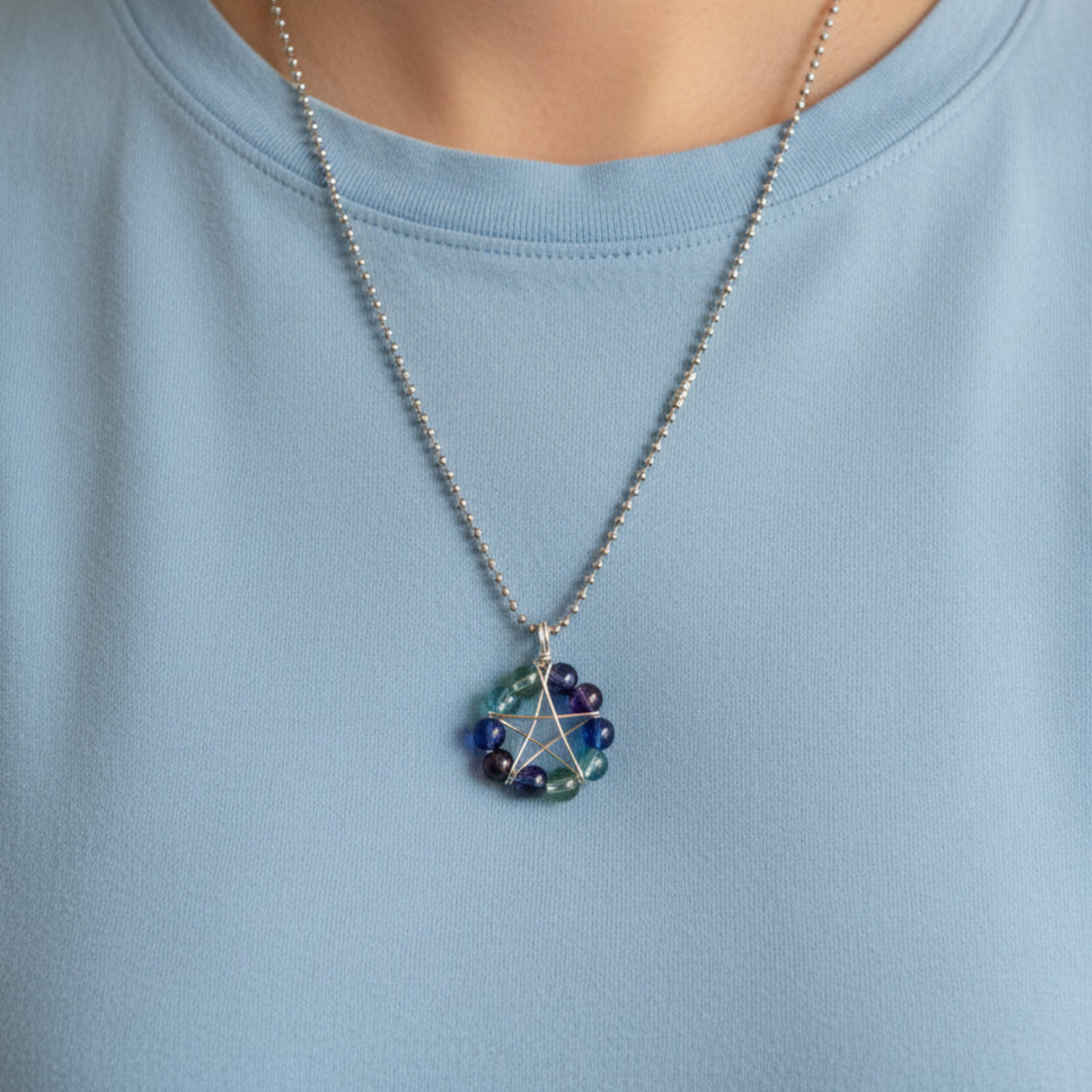 Necklace with a aqua colorful bead pendant wire wrapped into a pentagram being worn by someone with a lite blue shirt