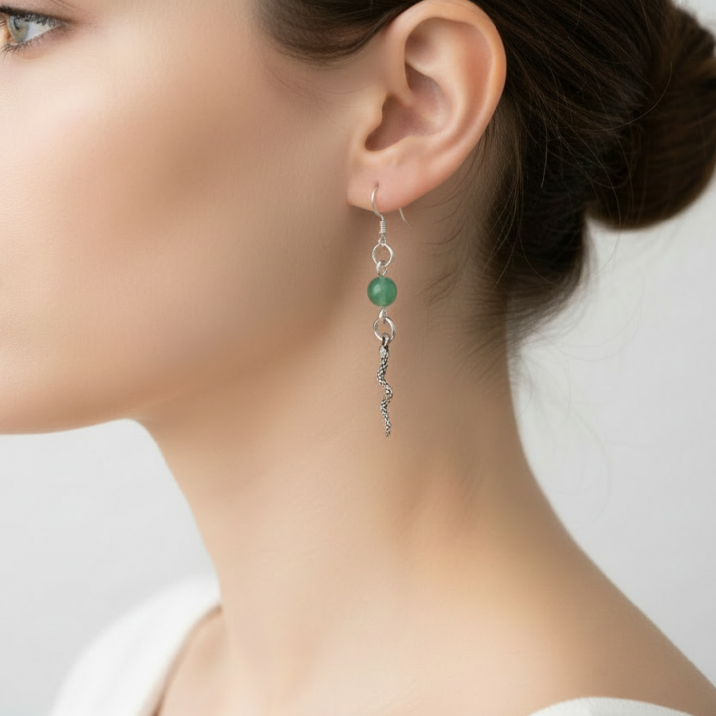 Close-up of a woman wearing a silver tone earring with a green aventurine gemstone bead with a silver tone snake displayed on a neutral background