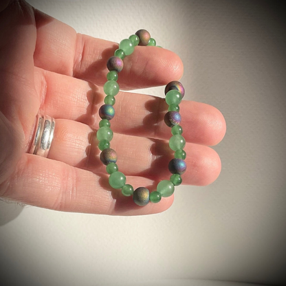Green aventurine beaded bracelet with purple tone druzy accents being held in a hand against a neutral background