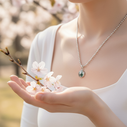 Person holding cherry blossoms wearing a Goddess Bastet charm pendant on a ball chain.