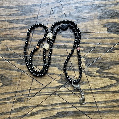 Black beaded necklace with cat beads and with a bronze tone Goddess cat pendant displayed on a wooden surface with a Pentagram etched into it
