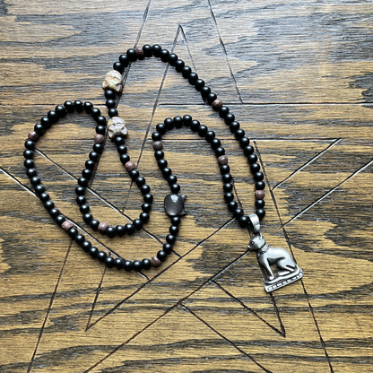 Black beaded Bastet necklace with a silver tone Bastet  pendant displayed on a wooden surface with a pentagram etched in to it