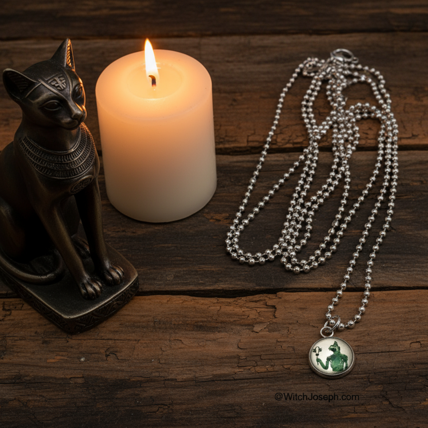 Goddess Bastet Necklace with a pendant next to a lit candle and Bastet cat statue on a wooden surface.