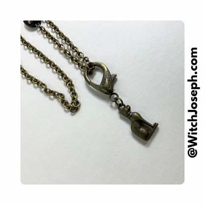 A bronze-toned necklace with a cat-shaped pendant lobster claw and a detachable chain. The brand's website is visible in the corner.