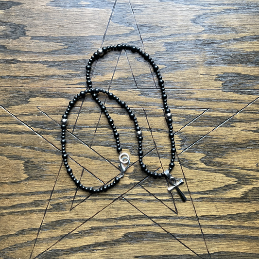 Necklace with black beads and silver accent beads and silver clasp with a stainless steel ankh pendant displayed on a wooden surface with a pentagram etched into it