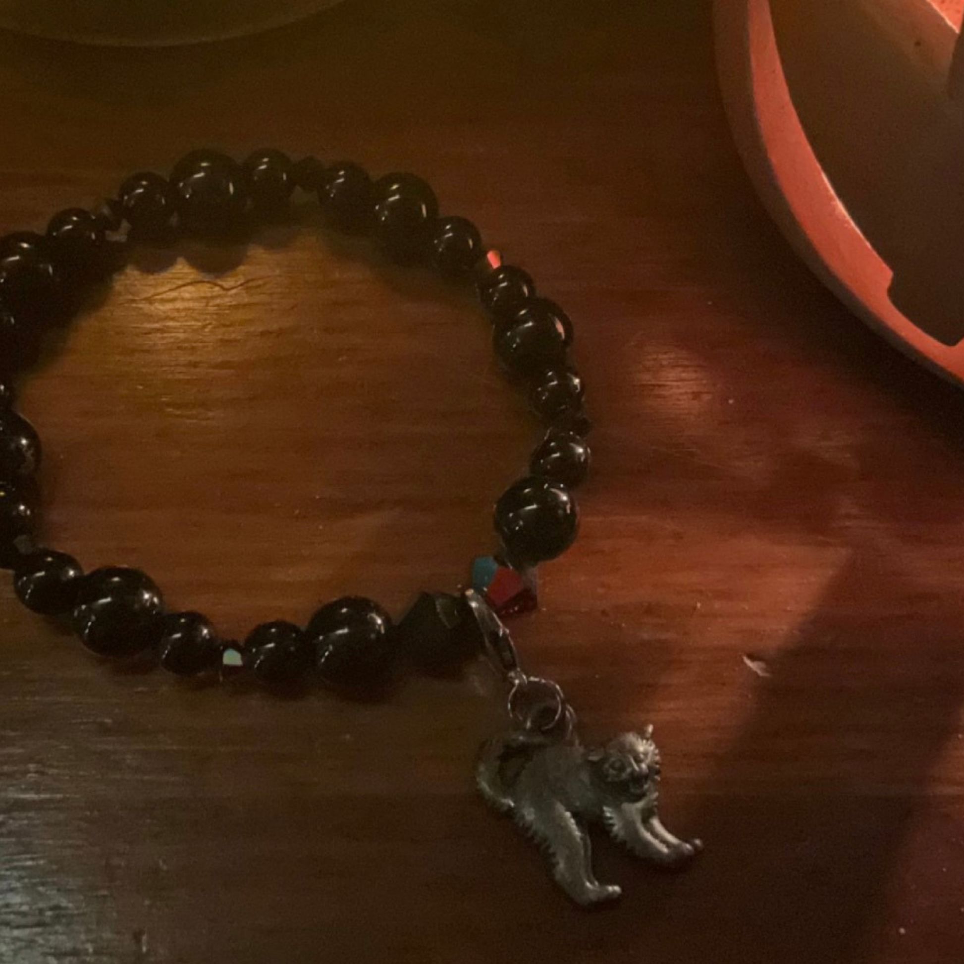 Black beaded bracelet with a black cat charm displayed on a wooden surface with halloween candle light