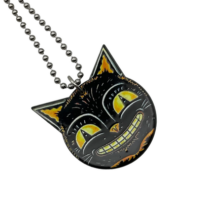 Front side of the vintage style Black cat grinning face  pendant with yellow accents on a ball chain against a white background