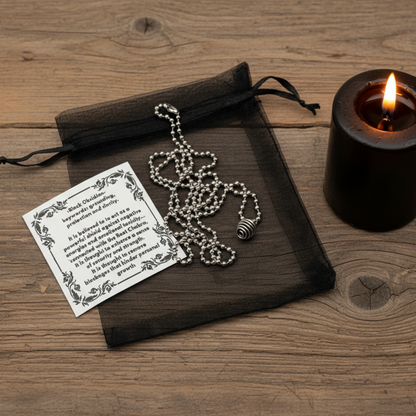 Necklace with black obsidian cage pendant next to a black candle on a wooden surface