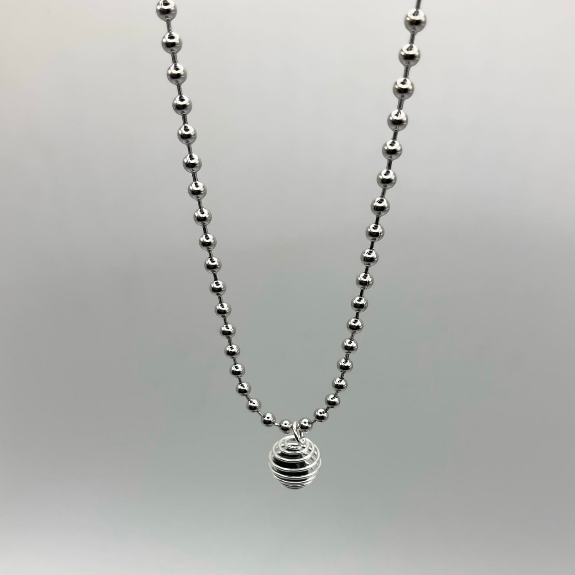 silver tone ball chain with black obsidian chip cage on grey background