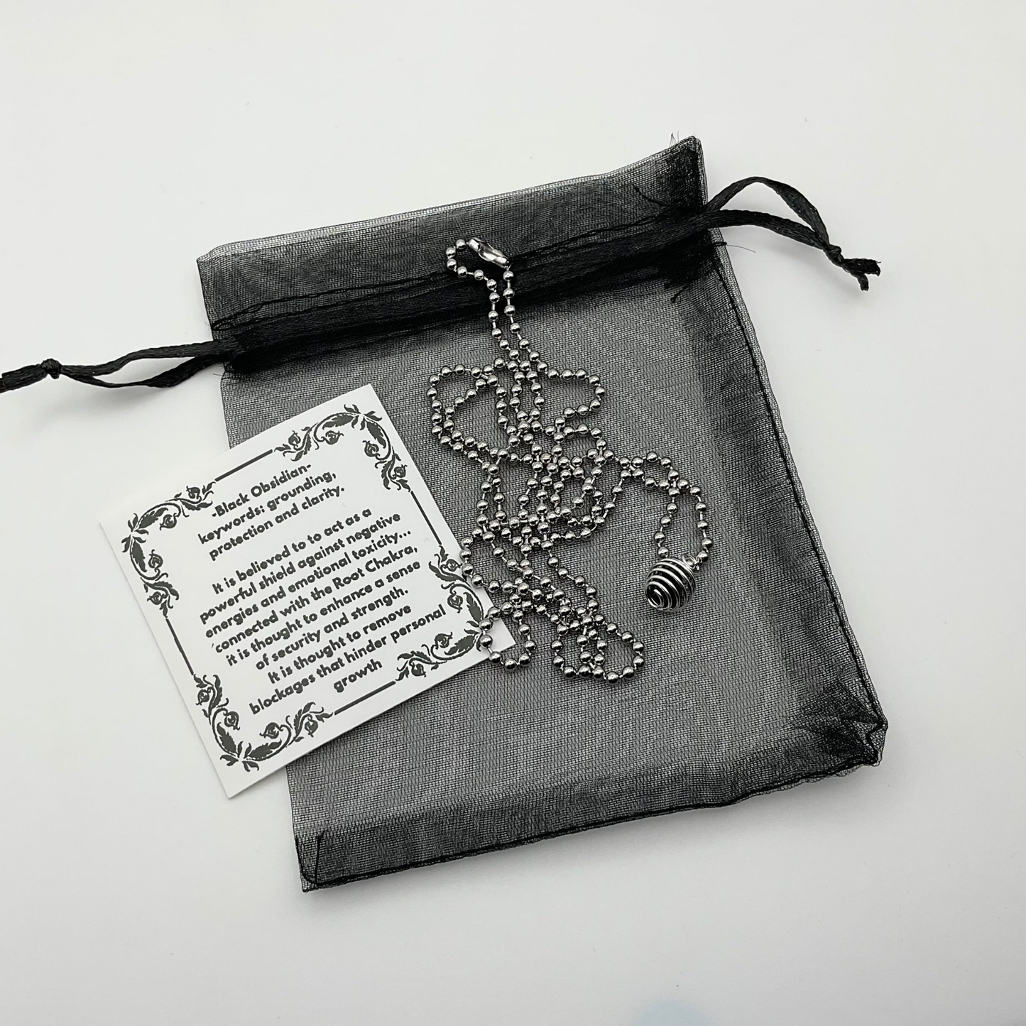 Necklace with a black chip obsidian cage pendant in a black organza drawstring bag on a white background