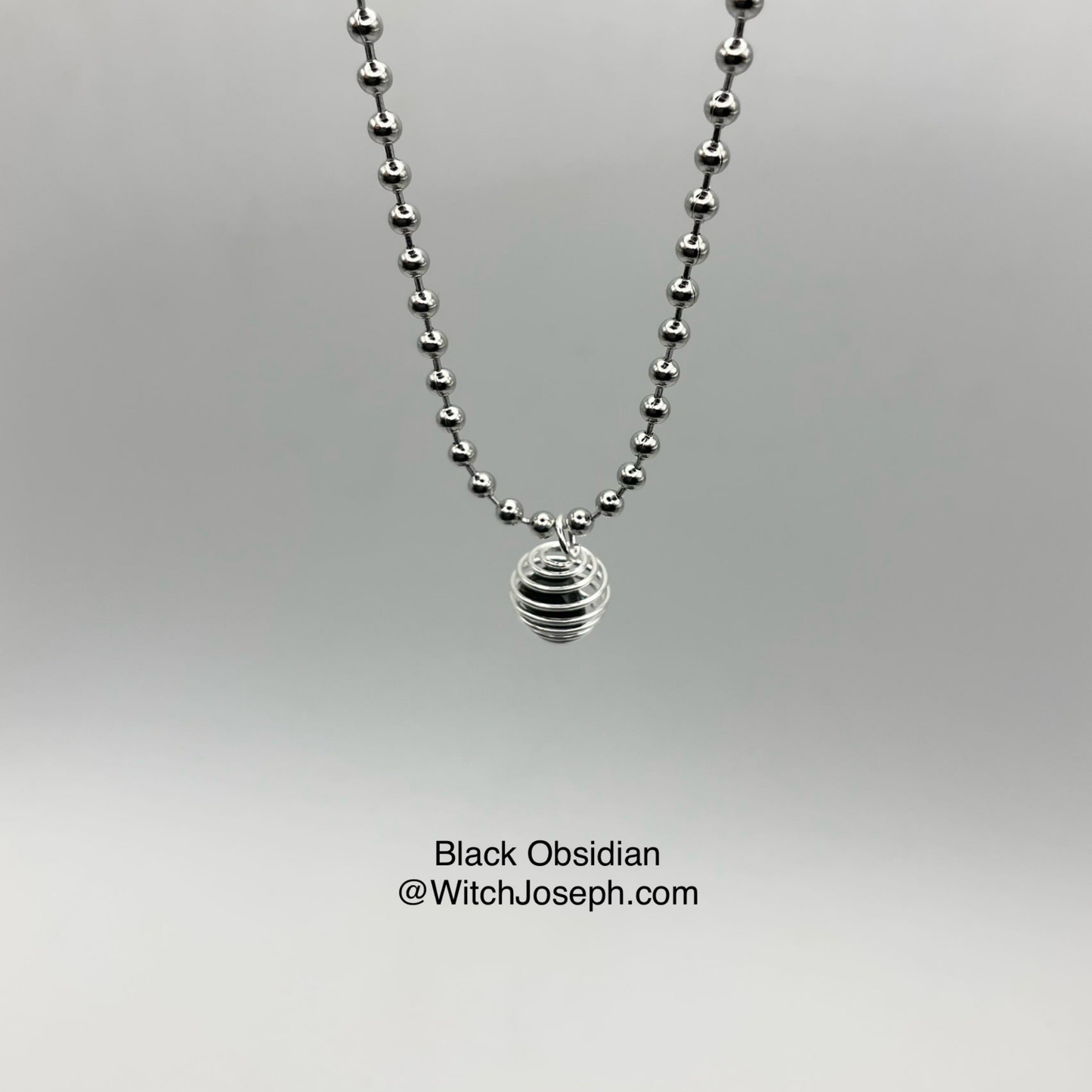 Silver ball chain necklace with a black obsidian chip cage pendant on a gray background