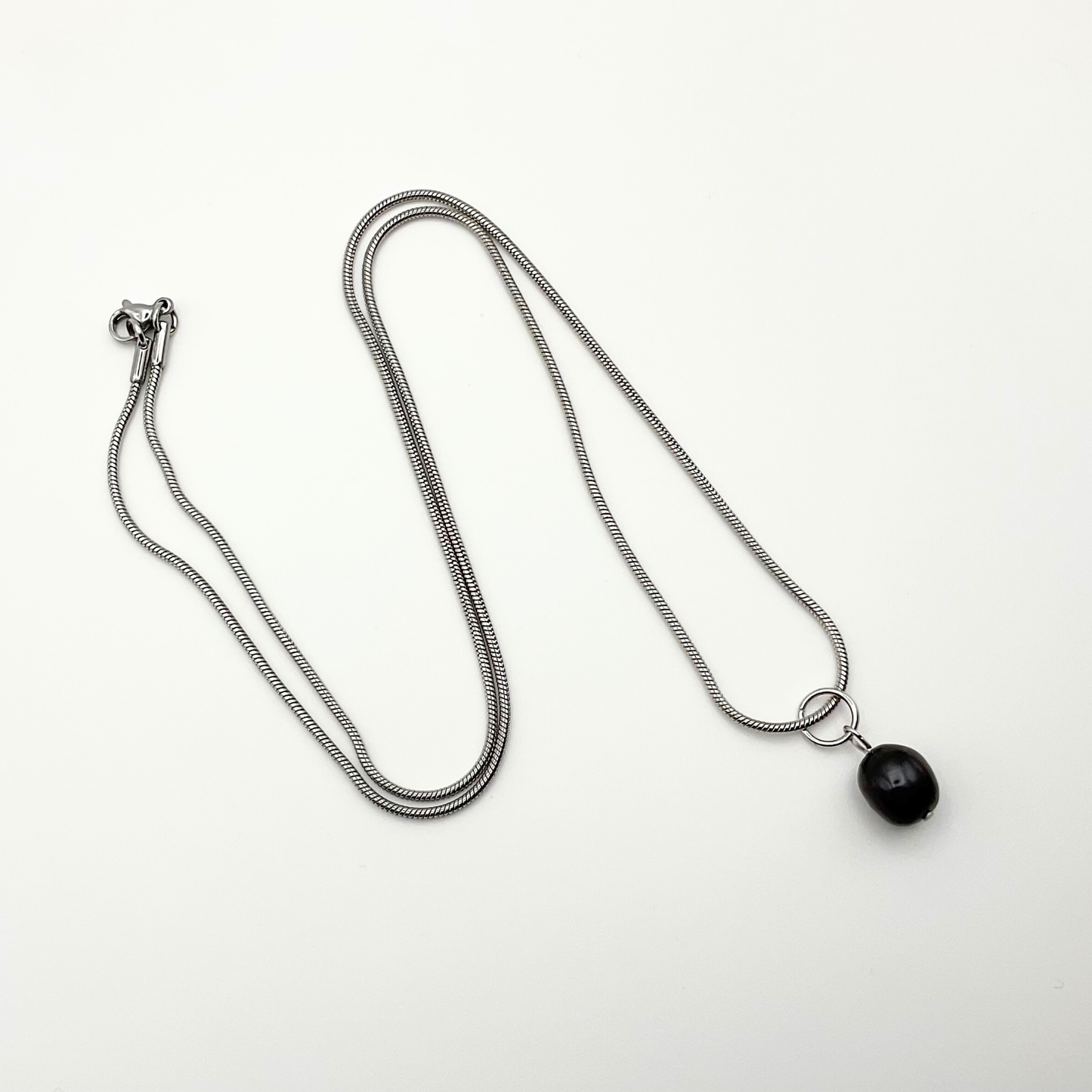 Silver tone necklace with a black pearl pendant on a white background