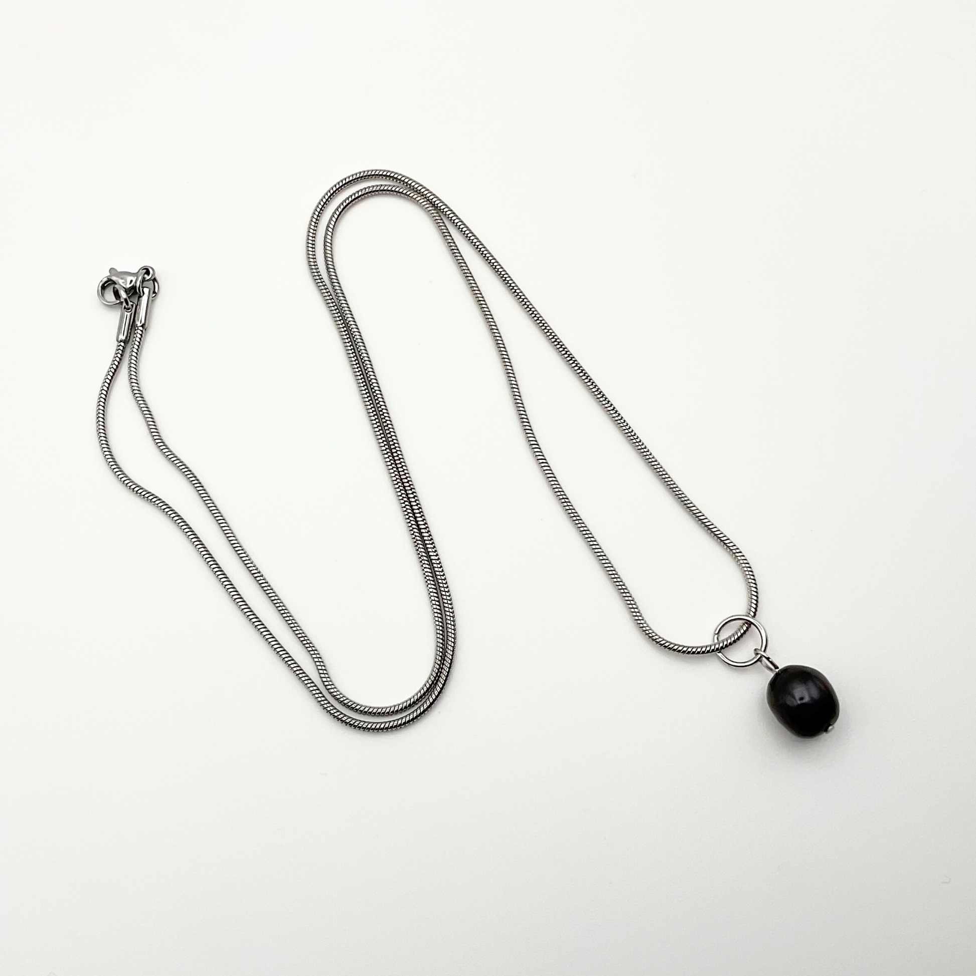 Silver tone necklace with a black pearl pendant on a white background