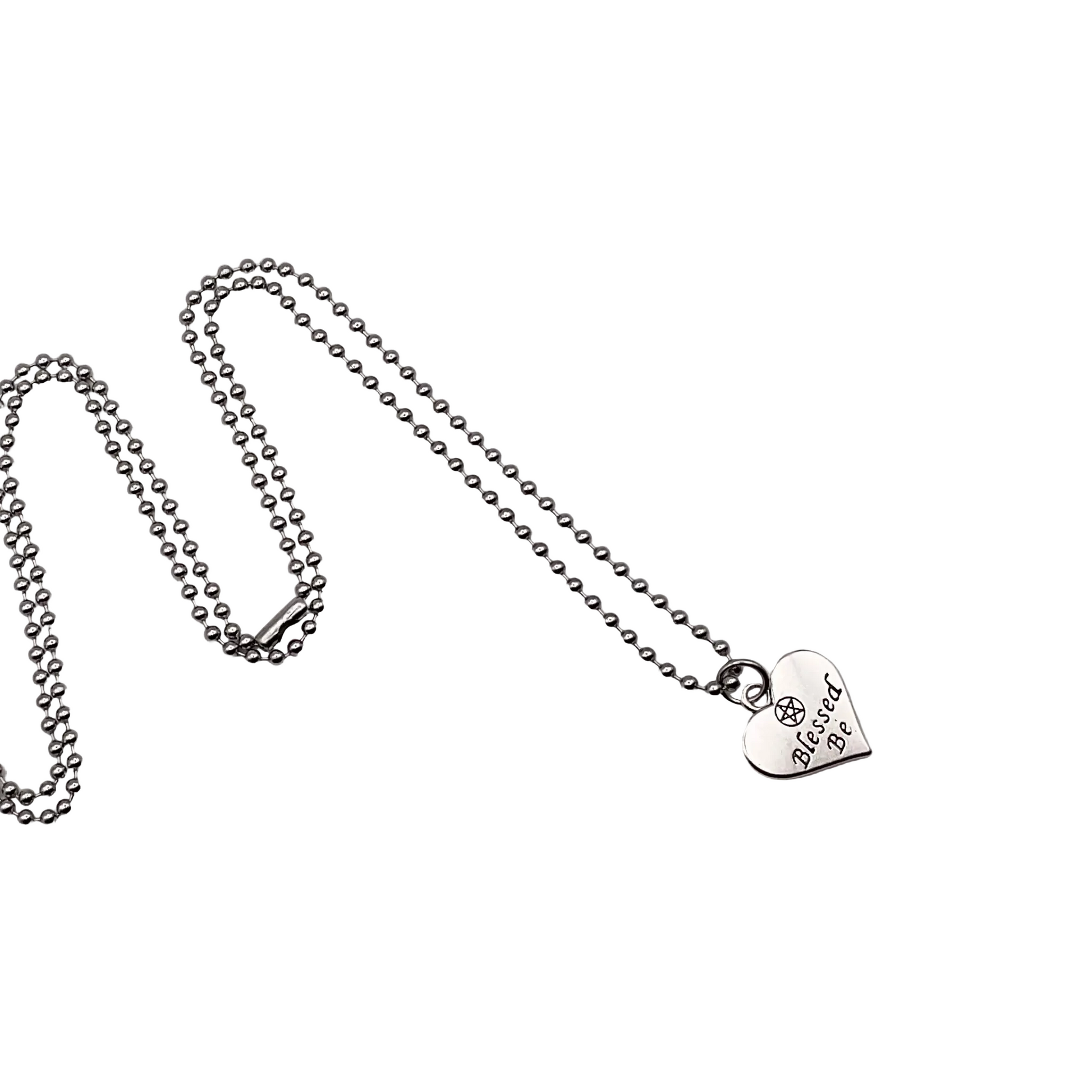 Silver tone necklace with a heart-shaped pendant with the words Blessed Be on it displayed on a white background.