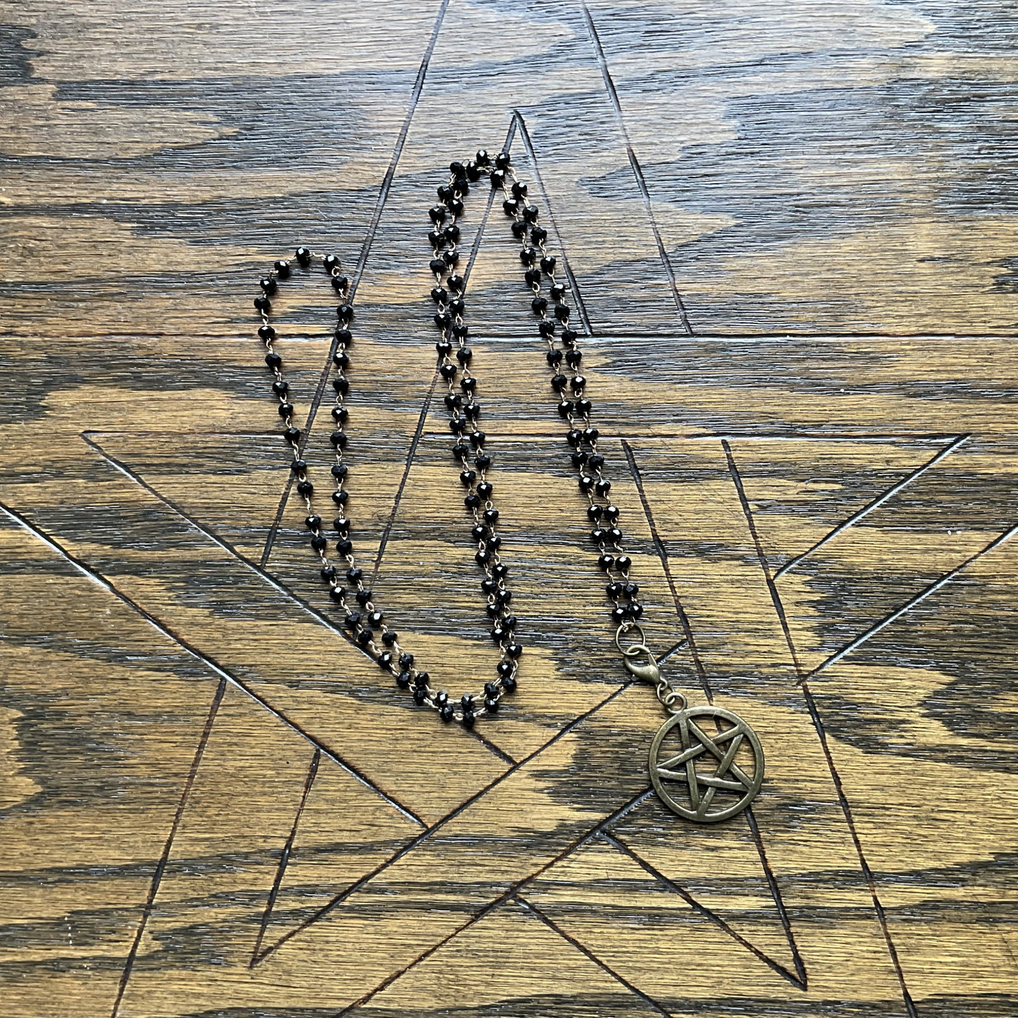 Bronze tone pentacle necklace on a sparkle bead chain displayed on a wooden surface with a pentagram etched into it