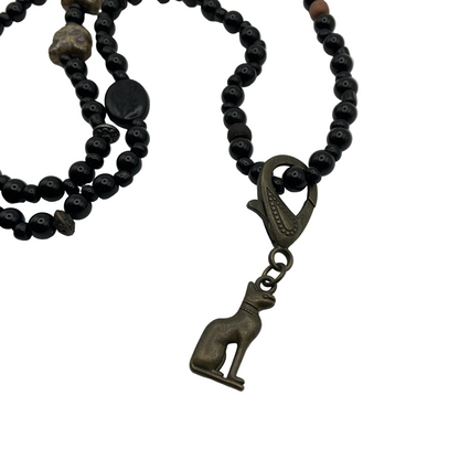 Black beaded necklace with cat beads and with a bronze cat pendant on a white background