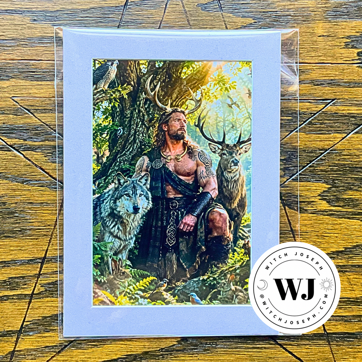 A matted art print featuring a fantasy illustration of Cernunnos with antlers sitting in a forest with a wolf and deer, displayed on a wooden surface with a circular 'Witch Joseph' logo.