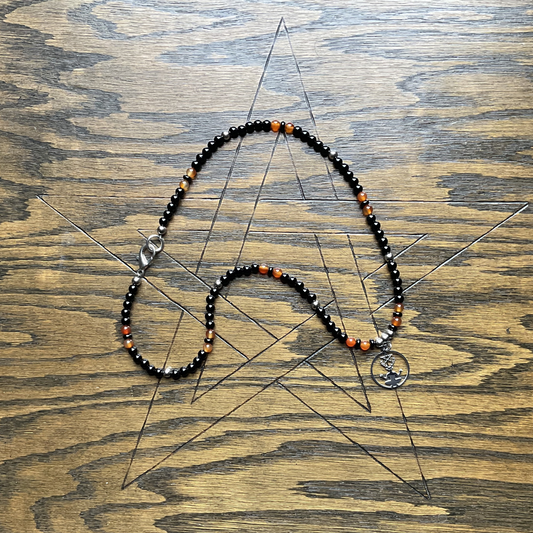 Necklace with black, orange, and silver beads on a wooden surface with a pentagram etched into it